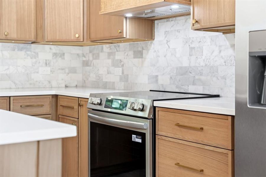 Kitchen featuring light wood cabinetry with gold-tone hardware, white countertops, and a subway tile backsplash