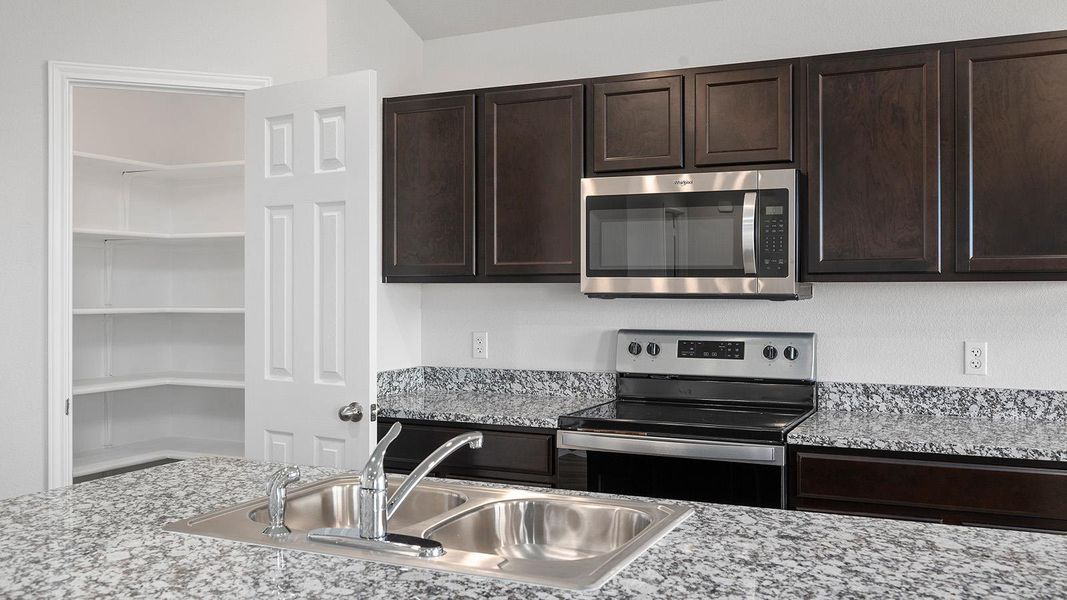 Kitchen with stainless steel appliances, dark brown cabinetry, and light stone counters