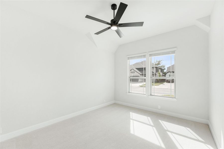 Empty bedroom with vaulted ceiling, black ceiling fan, carpet flooring, and large window with neighborhood view
