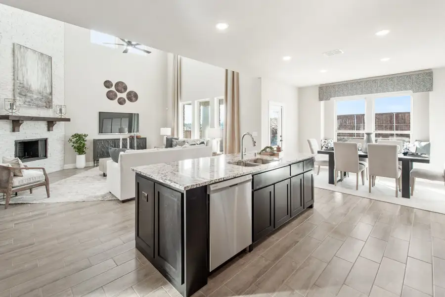 Open-concept kitchen with dark island, granite countertop, and views of living and dining areas with fireplace Open-concept kitchen with dark island, granite countertop, and views of living and dining areas with fireplace