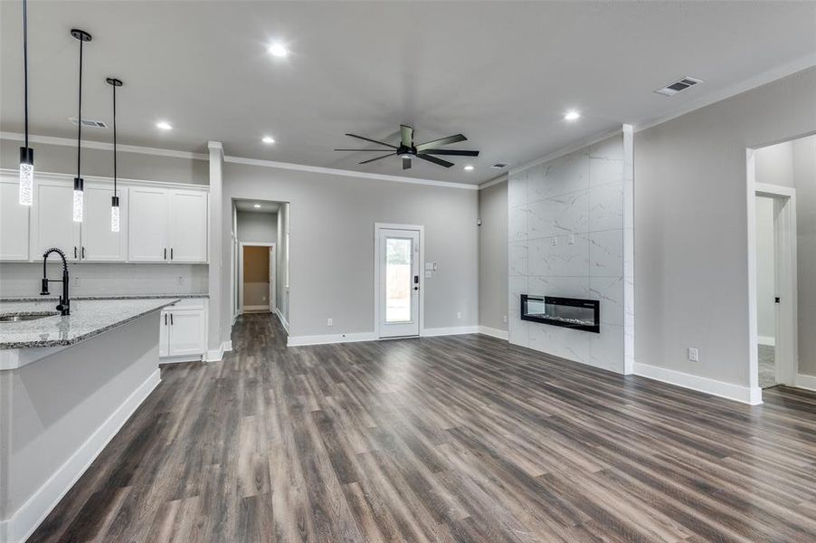 Unfurnished living room with dark wood-style floors, a ceiling fan, recessed lighting, a premium fireplace, and ornamental molding Unfurnished living room with dark wood-style floors, a ceiling fan, recessed lighting, a premium fireplace, and ornamental molding