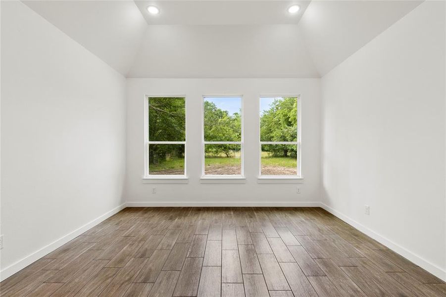 Vaulted ceiling room featuring three large windows, wood-finish flooring, recessed lighting, and crisp white walls with matching baseboards