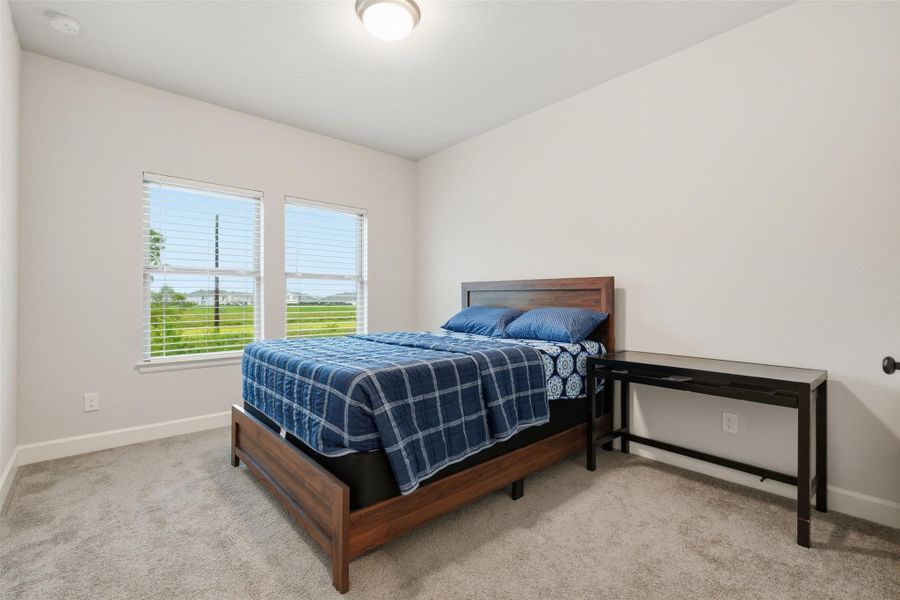 This bright bedroom features two large windows, neutral walls, and carpeted flooring. It includes a wooden bed with blue bedding and a modern side table, offering a cozy and inviting atmosphere. This bright bedroom features two large windows, neutral walls, and carpeted flooring. It includes a wooden bed with blue bedding and a modern side table, offering a cozy and inviting atmosphere.