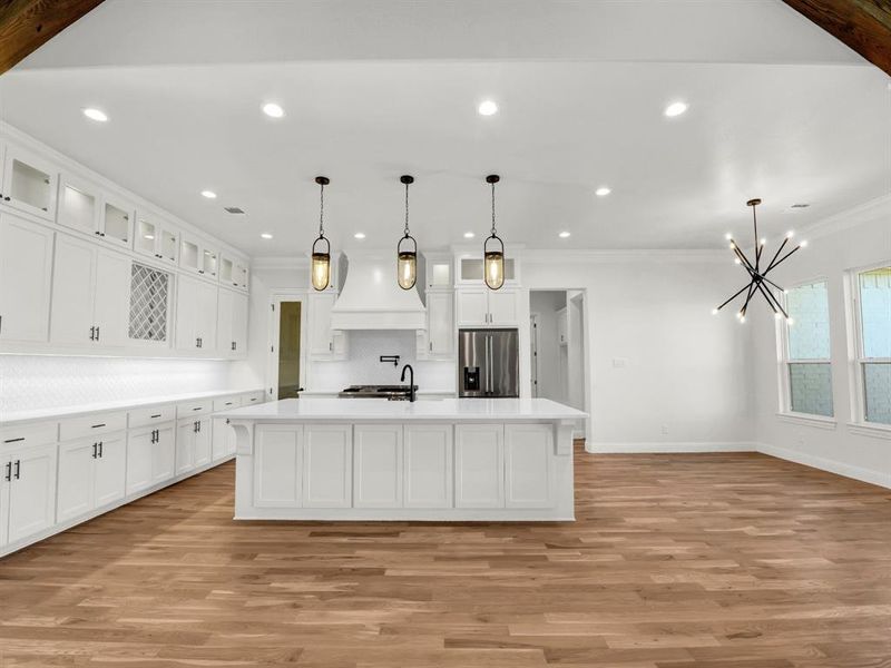 Kitchen featuring appliances with stainless steel finishes, light wood-type flooring, ornamental molding, a kitchen island with sink, and pendant lighting