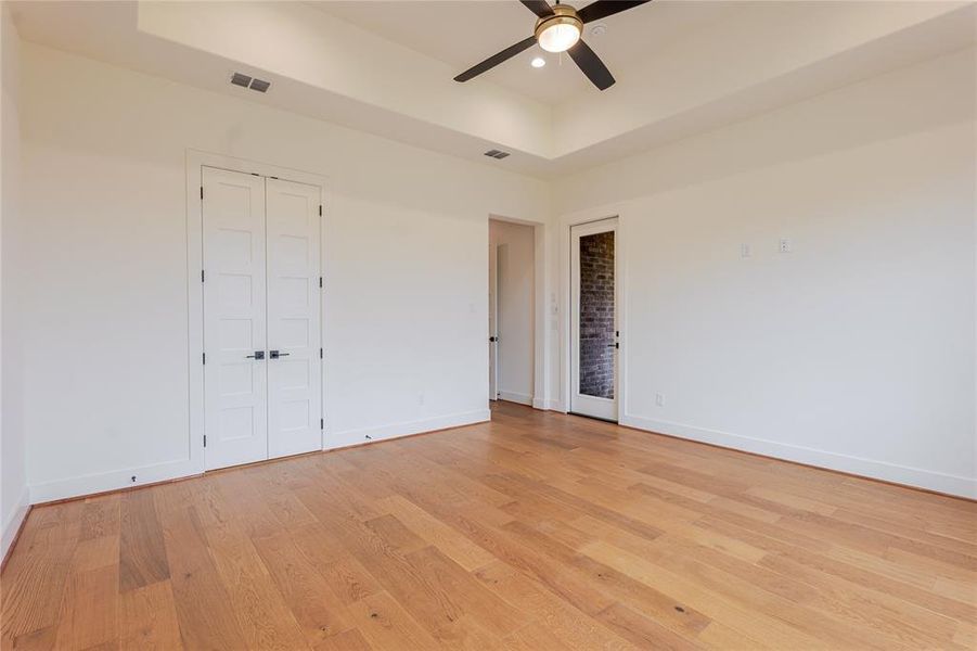 Unfurnished bedroom featuring a tray ceiling, a ceiling fan, light wood-style floors, recessed lighting, and a closet