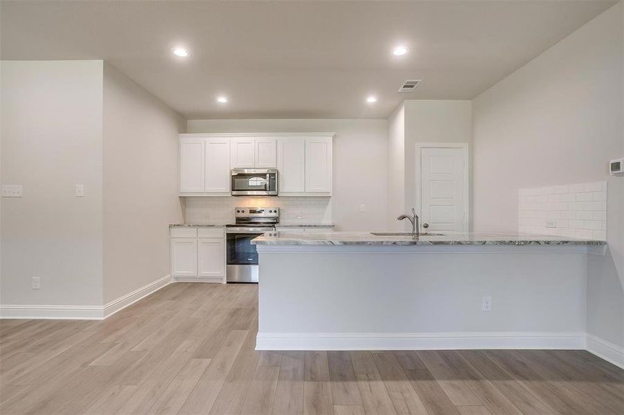 Kitchen featuring tasteful backsplash, a peninsula, white cabinets, light stone counters, and stainless steel appliances Kitchen featuring tasteful backsplash, a peninsula, white cabinets, light stone counters, and stainless steel appliances