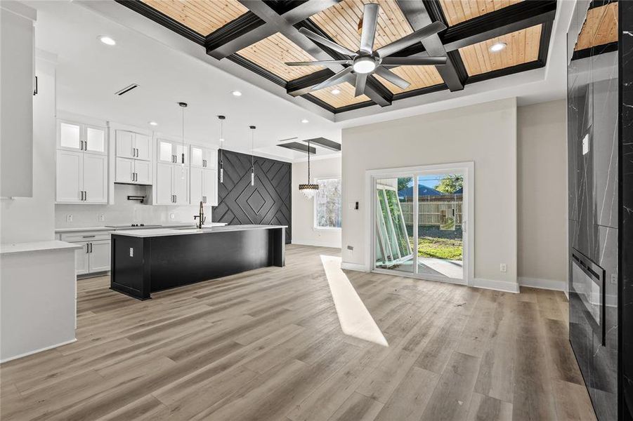 Kitchen featuring coffered ceiling, hanging light fixtures, light wood-type flooring, an island with sink, and white cabinetry