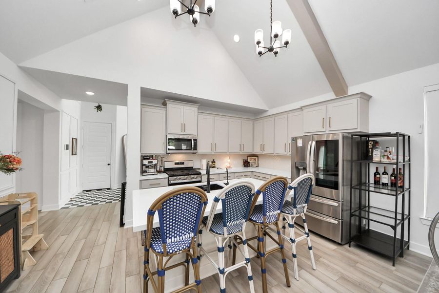 This modern kitchen features high vaulted ceilings, sleek cabinets, and stainless steel appliances. It includes a spacious island with seating, wood-look flooring, and stylish lighting fixtures, offering a bright and inviting space for cooking and entertaining. This modern kitchen features high vaulted ceilings, sleek cabinets, and stainless steel appliances. It includes a spacious island with seating, wood-look flooring, and stylish lighting fixtures, offering a bright and inviting space for cooking and entertaining.