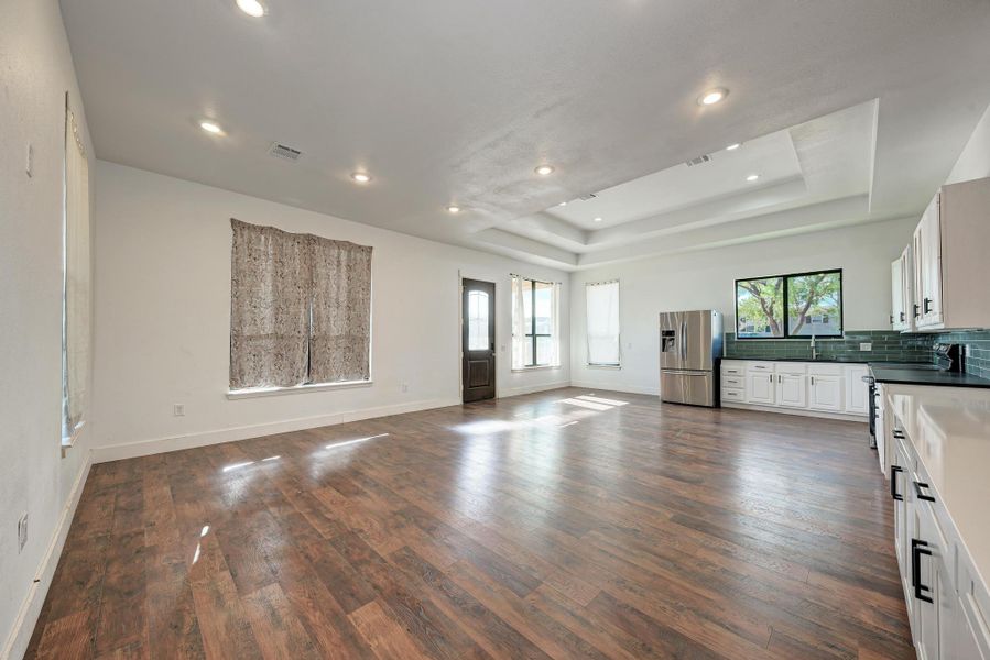 Rich wood-look flooring anchors a modern open layout beneath a detailed tray ceiling.