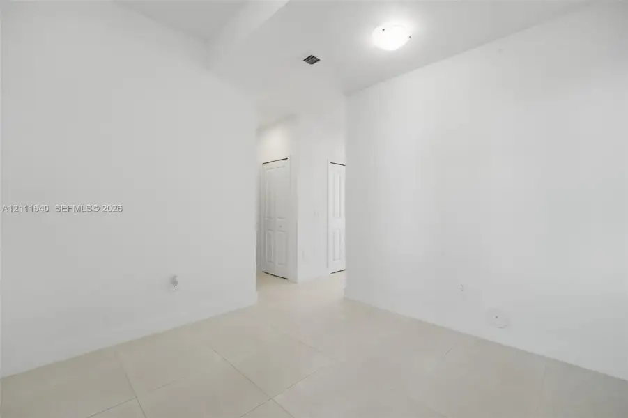 Neutral interior space featuring large-format ceramic tile flooring, crisp white walls, and two multi-panel interior doors