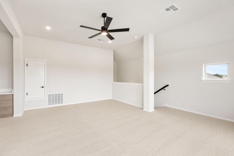 Open upstairs bonus room with carpet, black ceiling fan, and staircase opening along the wall.