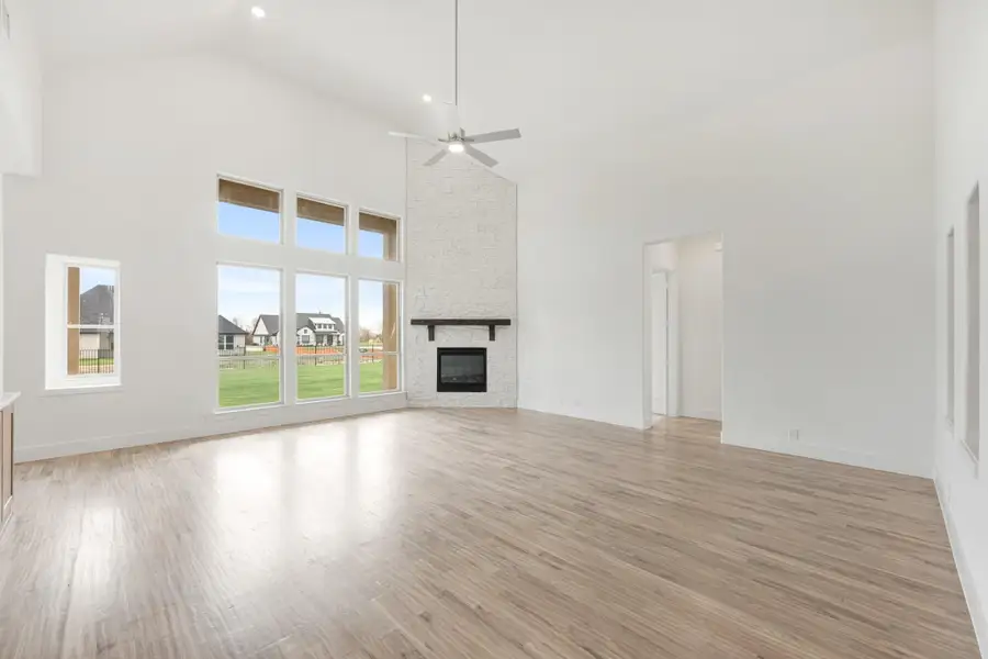 Open living room with vaulted ceiling, white brick fireplace, hardwood floors, and large windows Open living room with vaulted ceiling, white brick fireplace, hardwood floors, and large windows