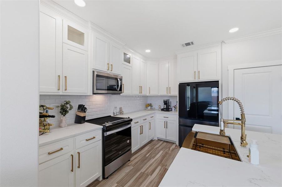 Kitchen featuring stainless steel appliances, white cabinetry, light wood finished floors, glass fronted cabinets, and recessed lighting