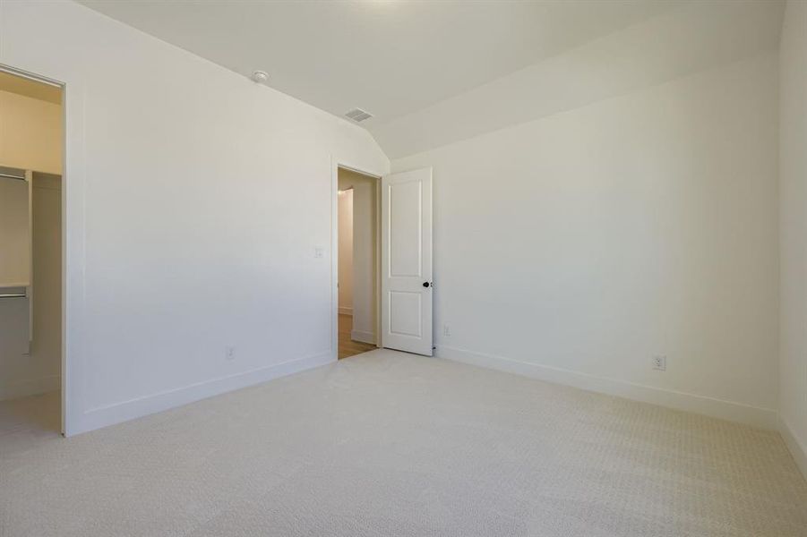 Unfurnished bedroom with a walk in closet, light carpet, and lofted ceiling Unfurnished bedroom with a walk in closet, light carpet, and lofted ceiling