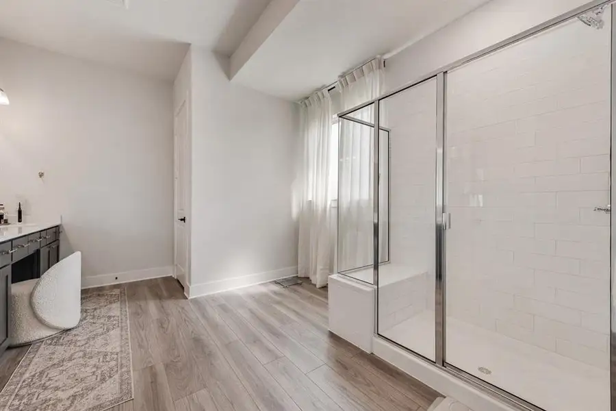 Spacious bathroom featuring a frameless glass shower enclosure with white subway tile, an integrated shower bench, and wood-finish flooring