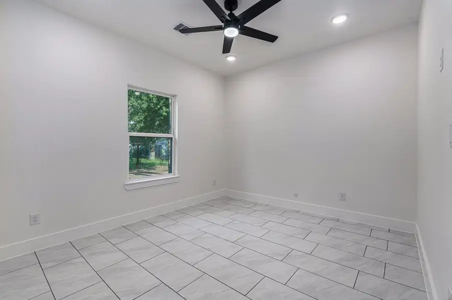 This room features neutral-toned tile flooring, a large window allowing natural light, and a modern ceiling fan with recessed lighting, creating a bright and airy space.