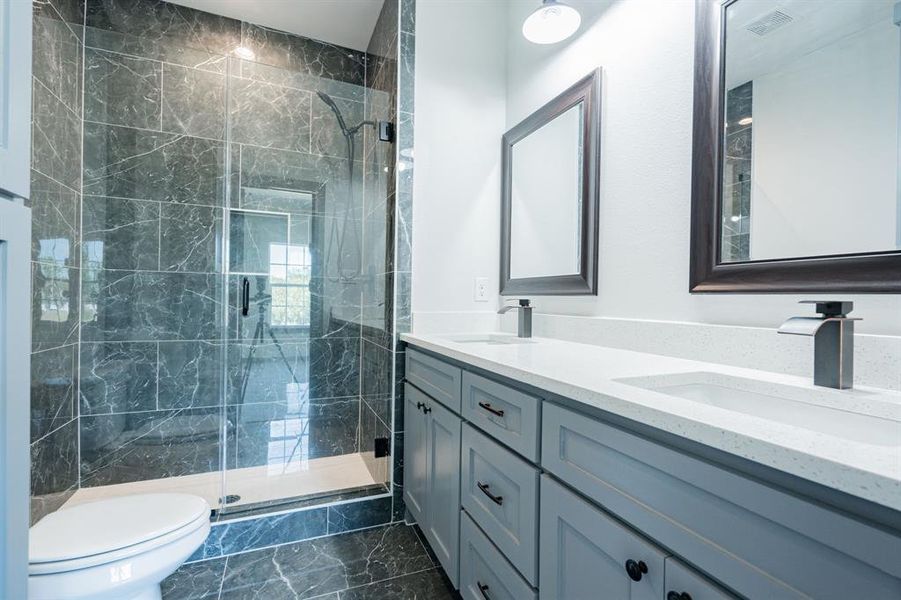 Bathroom with tile patterned flooring, a shower with door, dual vanity, and toilet