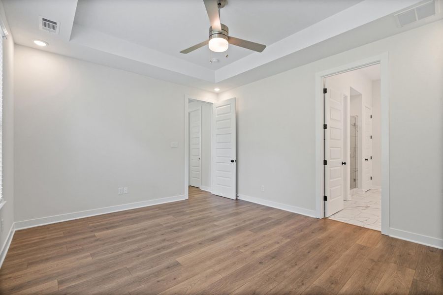 Spacious room with wood-finish flooring, crisp white walls, and a recessed ceiling with a contemporary ceiling fan Spacious room with wood-finish flooring, crisp white walls, and a recessed ceiling with a contemporary ceiling fan
