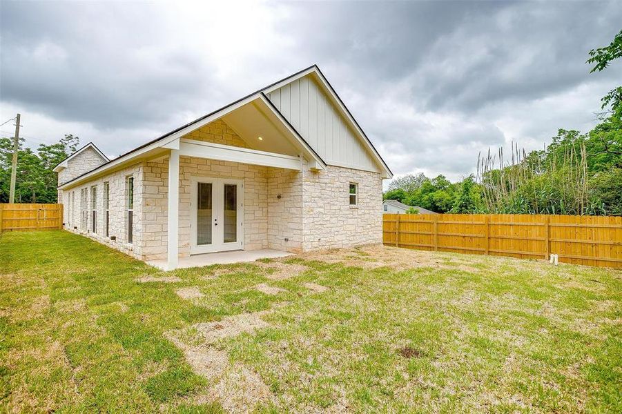 Rear view of property with board and batten siding, french doors, a fenced backyard, a yard, and stone siding Rear view of property with board and batten siding, french doors, a fenced backyard, a yard, and stone siding