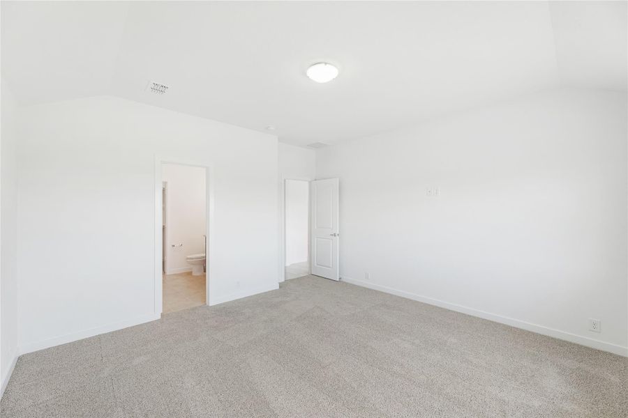 Empty bedroom with gray carpet, white walls, and an attached bathroom visible through open door