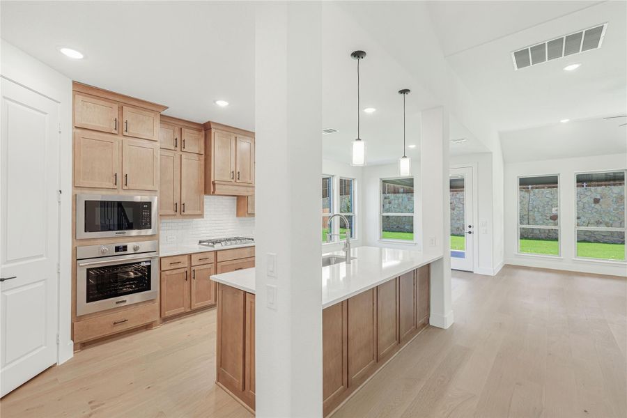 Kitchen with light wood cabinets, stainless steel appliances, white island, and pendant lights over open living area with hardwood floors Kitchen with light wood cabinets, stainless steel appliances, white island, and pendant lights over open living area with hardwood floors