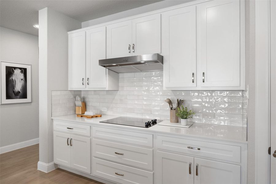 The kitchen showcases a tasteful tile backsplash, sleek under-cabinet range hood, and timeless white cabinetry—blending style and function in a clean, modern design.