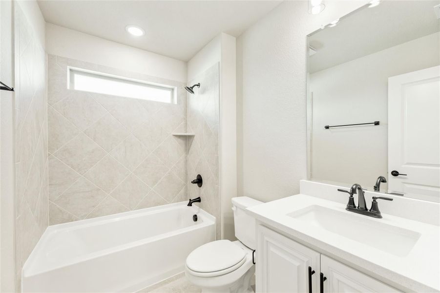 Bathroom with tiled tub and shower, white vanity, and black hardware fixtures Bathroom with tiled tub and shower, white vanity, and black hardware fixtures