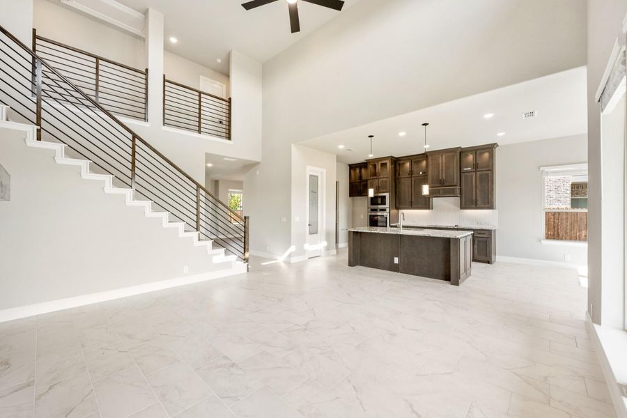 Open-concept living area with two-story ceiling, staircase, and kitchen with dark cabinets and island