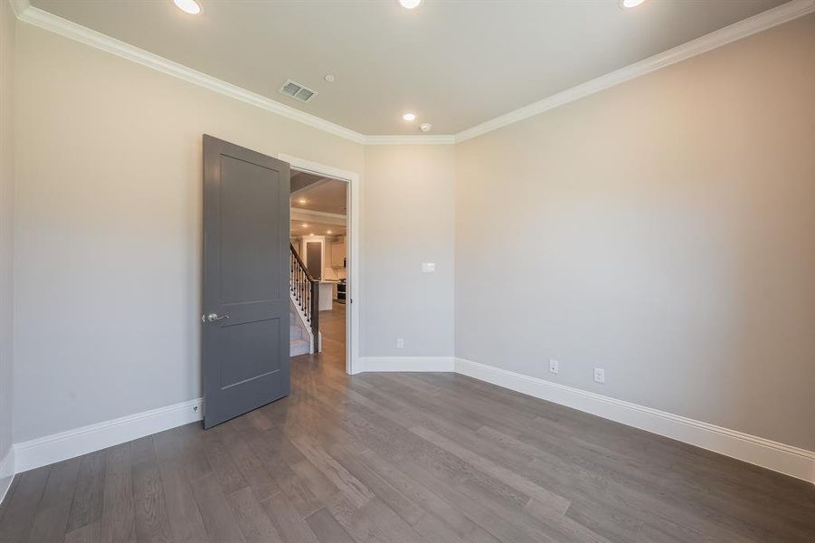 Room featuring wood-finish flooring, light gray wall paint, white crown molding, recessed lighting, and a dark gray interior door with a silver handle