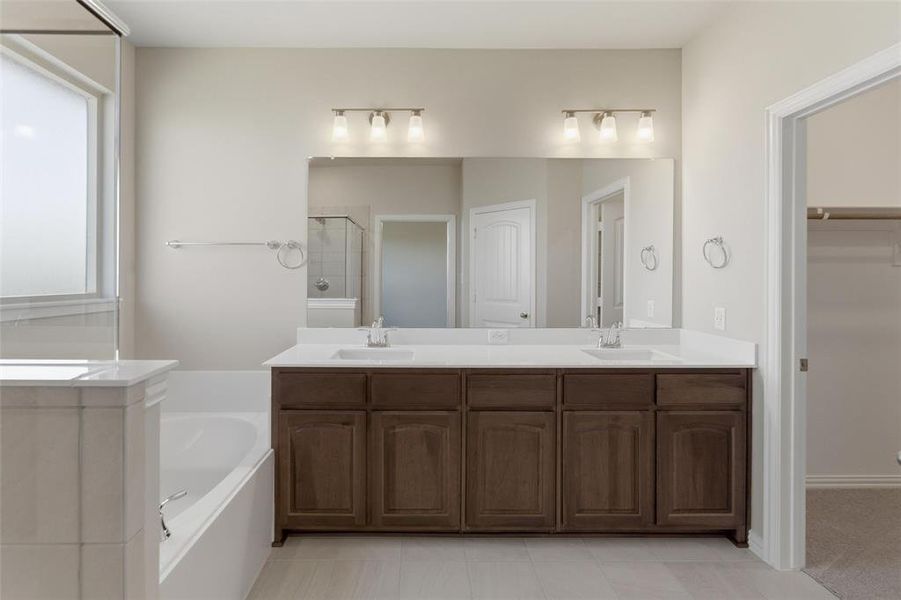 Full bathroom with double vanity, a garden tub, a stall shower, a walk in closet, and light tile patterned floors