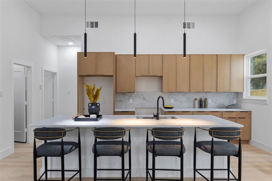 Kitchen with light wood-type flooring, modern cabinets, a kitchen bar, a towering ceiling, and a kitchen island with sink