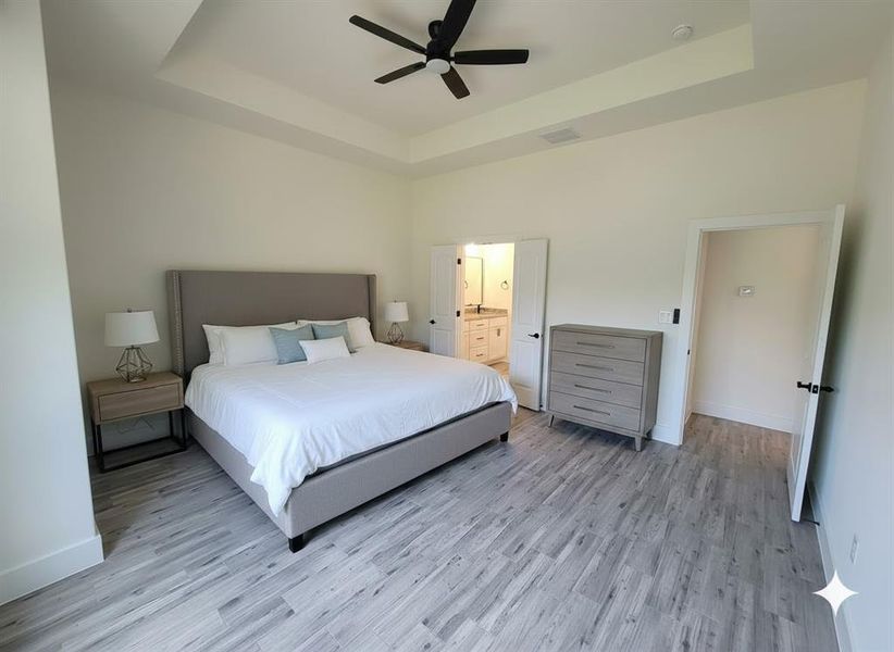 Spacious room featuring light-toned flooring, a tray ceiling, and a ceiling fan