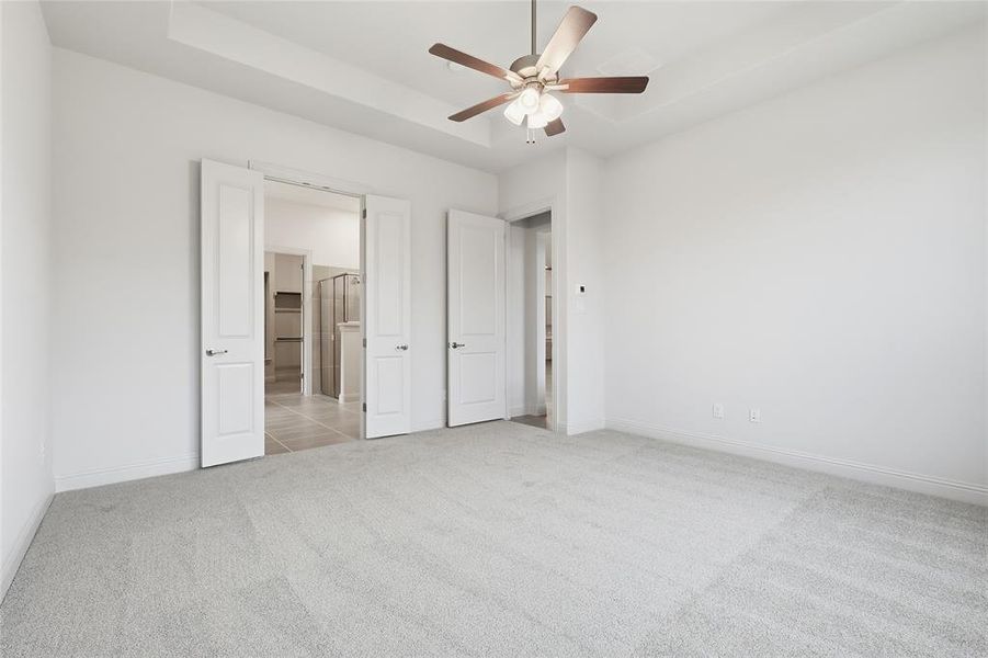 Unfurnished bedroom with light colored carpet, a raised ceiling, and ceiling fan