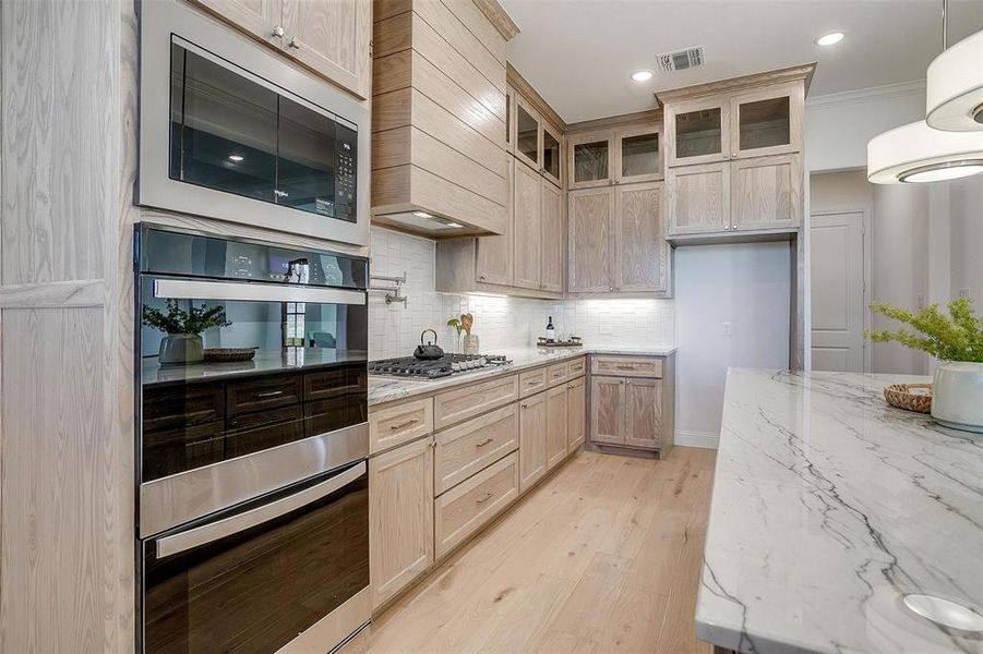 Kitchen featuring Quartzite countertops, tasteful backsplash, light hardwood / wood-style flooring, a kitchen island, and appliances with stainless steel finishes