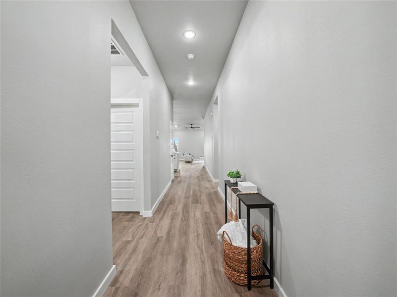 Long hallway featuring recessed lighting, wood-finish flooring, white baseboards, and light gray walls Long hallway featuring recessed lighting, wood-finish flooring, white baseboards, and light gray walls