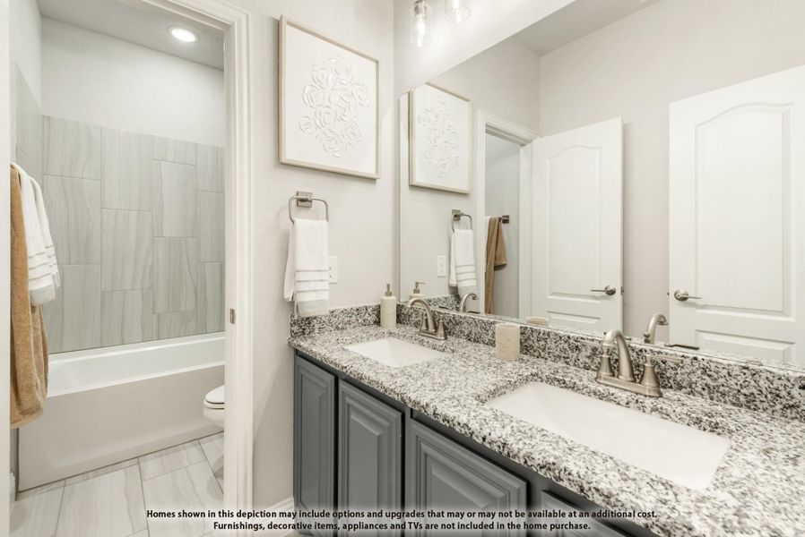 Bathroom with double granite vanity, gray cabinets, and tiled shower-tub combo