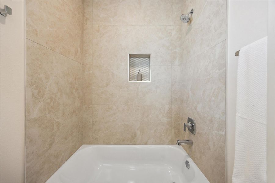 The secondary bath’s tub and shower combination is finished with large-format stone-look tile for a clean, timeless appeal.