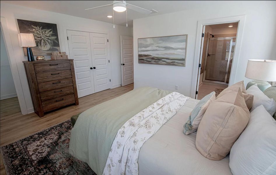 Bedroom featuring wood-finish flooring, a ceiling fan with integrated lighting, and a doorway opening to an en-suite bathroom with a glass-enclosed shower