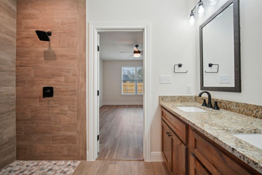 Full bathroom with double vanity, tiled shower, wood finished floors, a ceiling fan, and a sink