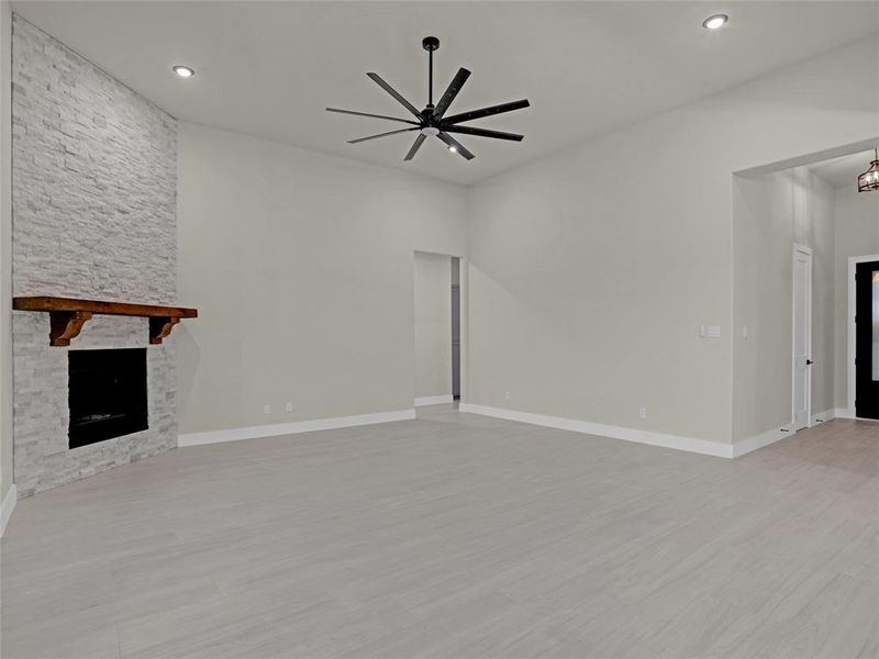 Unfurnished living room with a stone fireplace, light hardwood / wood-style flooring, and ceiling fan