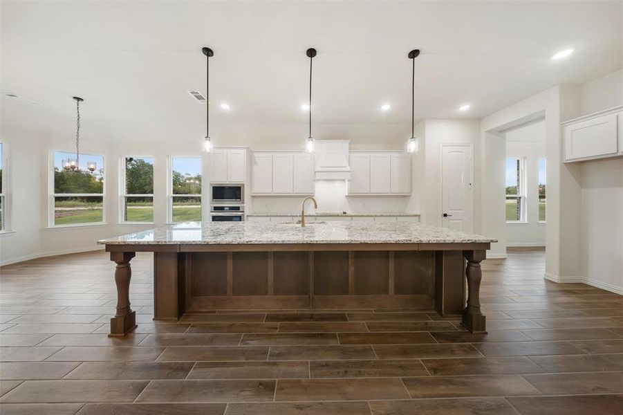 Kitchen featuring white cabinetry, a breakfast bar, wood tiled floors, a spacious island, and pendant lighting
