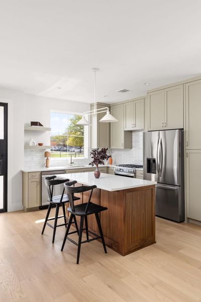 Kitchen with stainless steel appliances, a breakfast bar, light wood-style flooring, and a kitchen island