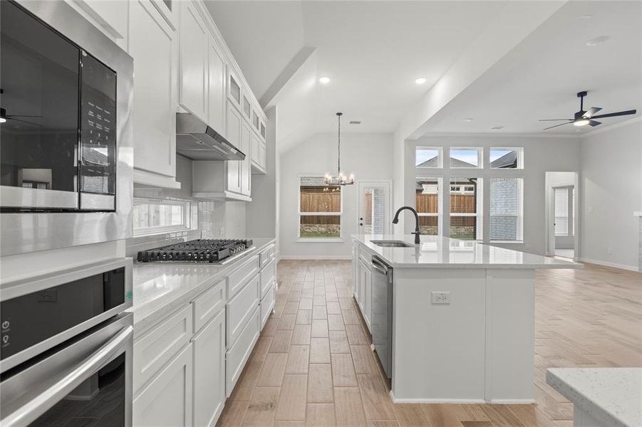 Kitchen featuring ventilation hood, sink, ceiling fan with notable chandelier, and an island with sink