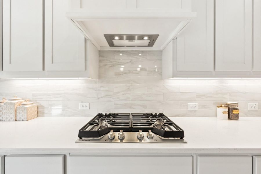 Kitchen cooktop area with stainless steel gas range, built-in hood vent, white cabinets, and marble tile backsplash Kitchen cooktop area with stainless steel gas range, built-in hood vent, white cabinets, and marble tile backsplash