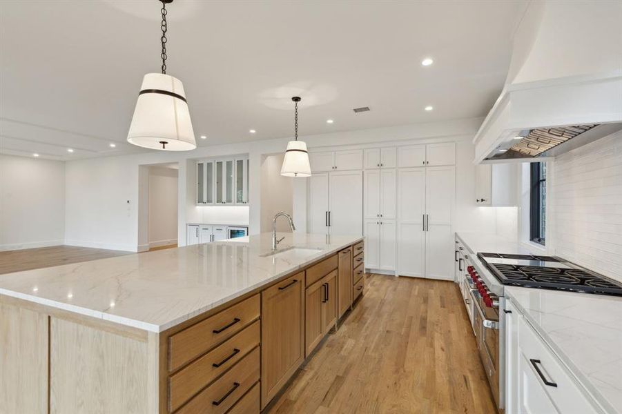 Kitchen with pendant lighting, sink, white cabinetry, high end stainless steel range, and a spacious island