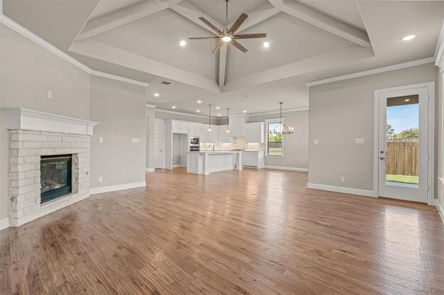 Unfurnished living room with beam ceiling, a stone fireplace, ceiling fan, light wood-type flooring, and a chandelier Unfurnished living room with beam ceiling, a stone fireplace, ceiling fan, light wood-type flooring, and a chandelier