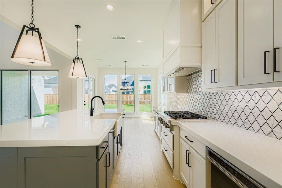 Kitchen with white cabinets, tasteful backsplash, decorative light fixtures, light wood finished floors, and recessed lighting Kitchen with white cabinets, tasteful backsplash, decorative light fixtures, light wood finished floors, and recessed lighting