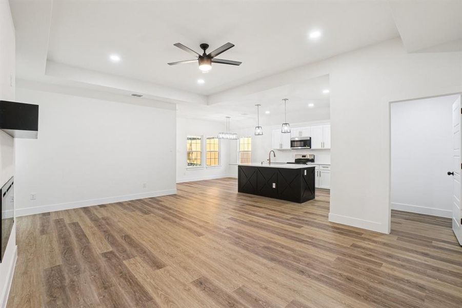 Unfurnished living room with a ceiling fan, recessed lighting, light wood-style floors, a raised ceiling, and a fireplace Unfurnished living room with a ceiling fan, recessed lighting, light wood-style floors, a raised ceiling, and a fireplace