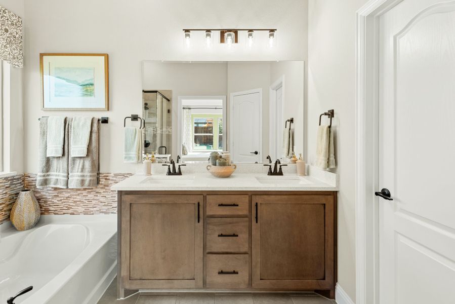Bathroom with double sink vanity, wood cabinets, white countertop, large mirror, and soaking tub with mosaic tile accent wall