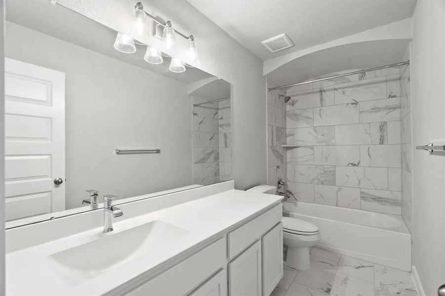 Experience sophistication in the secondary bathroom, where tile flooring complements a bath/shower combo with tile surround. Light-stained wood cabinets enhance the space, while a distinctive barrel ceiling adds a touch of architectural elegance. Sample photo of completed home with similar floor plan. As-built interior colors and selections may vary.